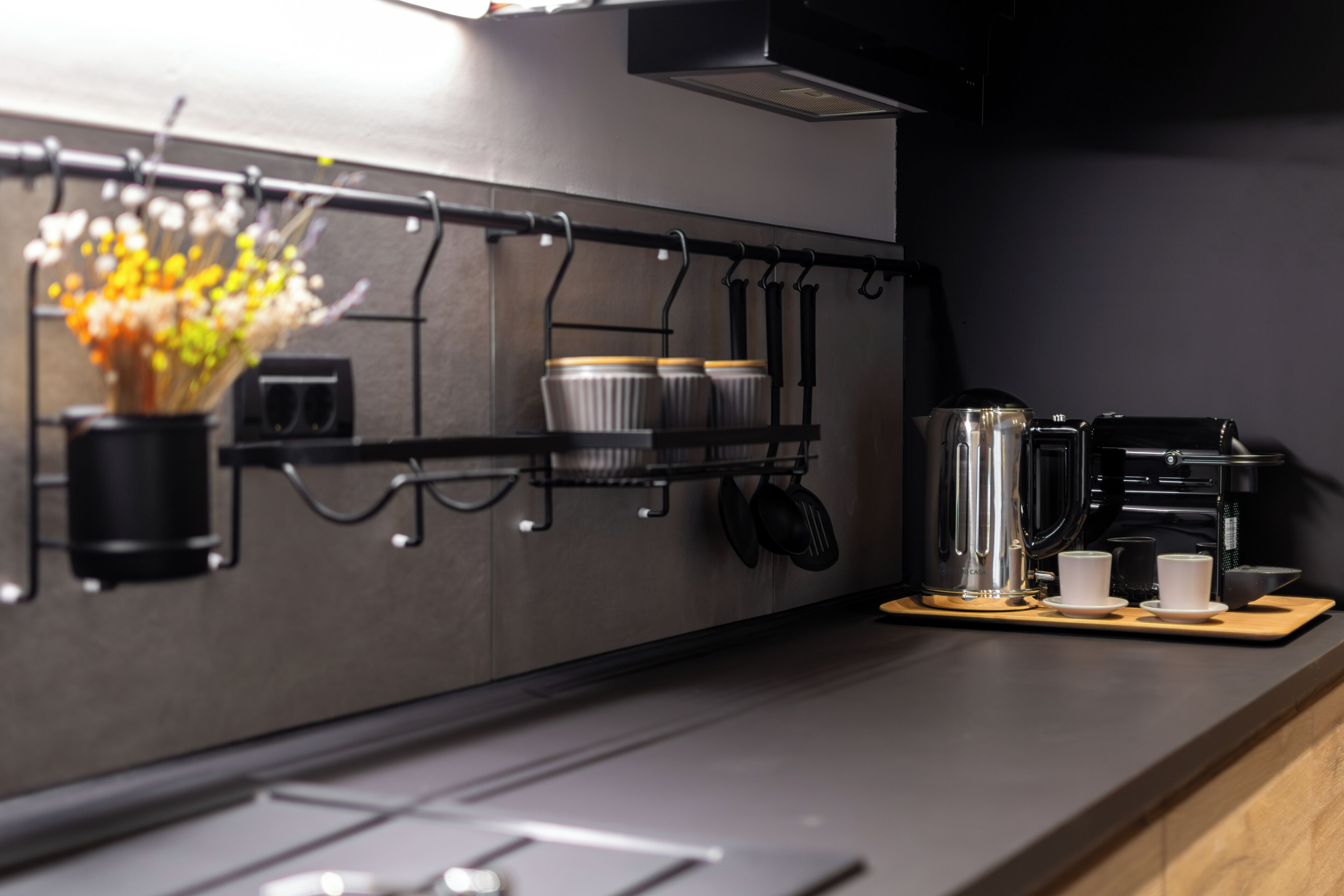 A modern kitchen with a black countertop, stainless steel appliances, and a hanging pot rack.