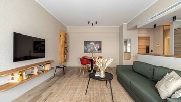 Uma sala de estar moderna com televisão de tela plana, um sofá verde, uma mesa de centro e um espaço de jantar com cadeiras vermelhas.