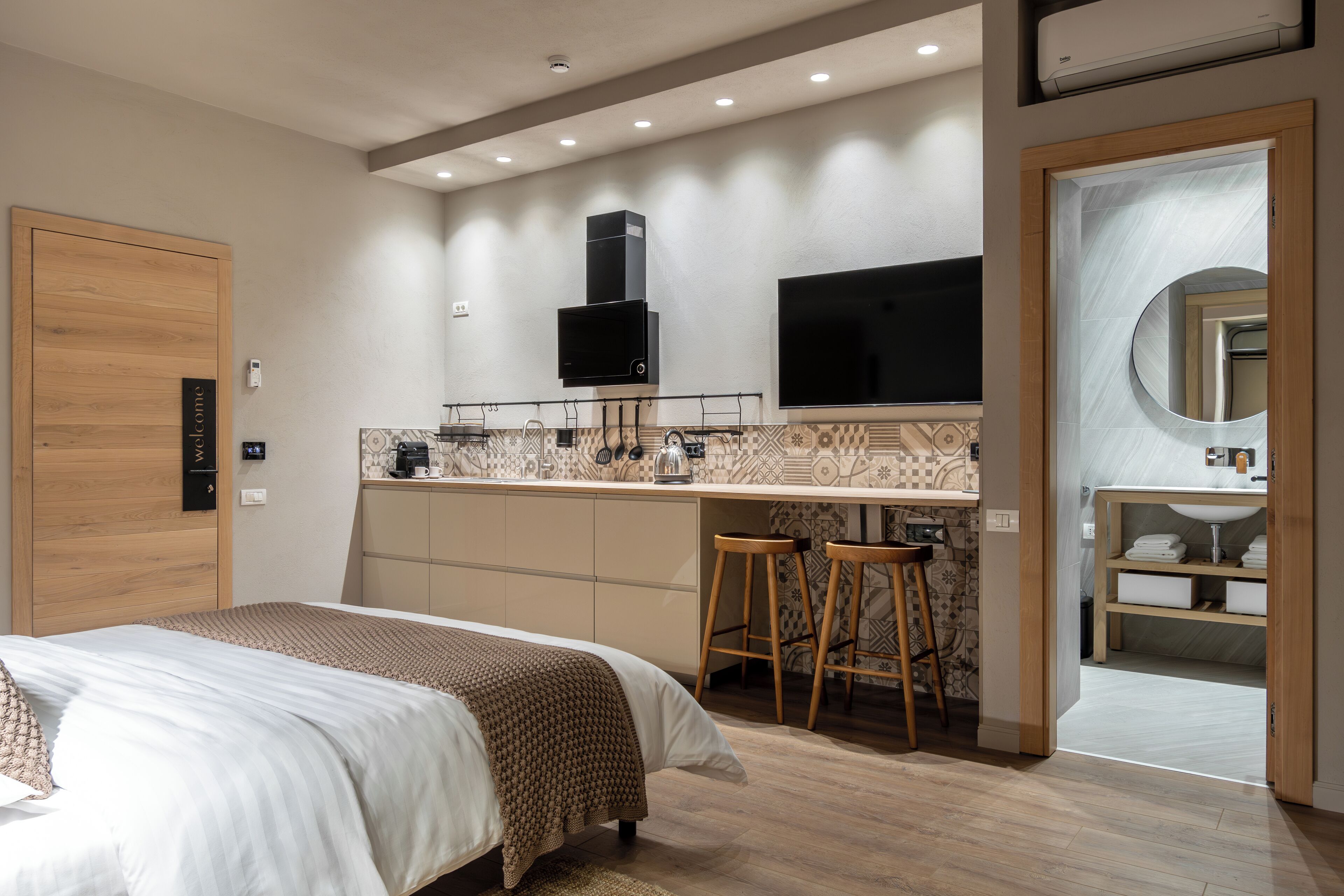 Una habitación de hotel moderna con cama, kitchenette, televisor y baño con espejo.