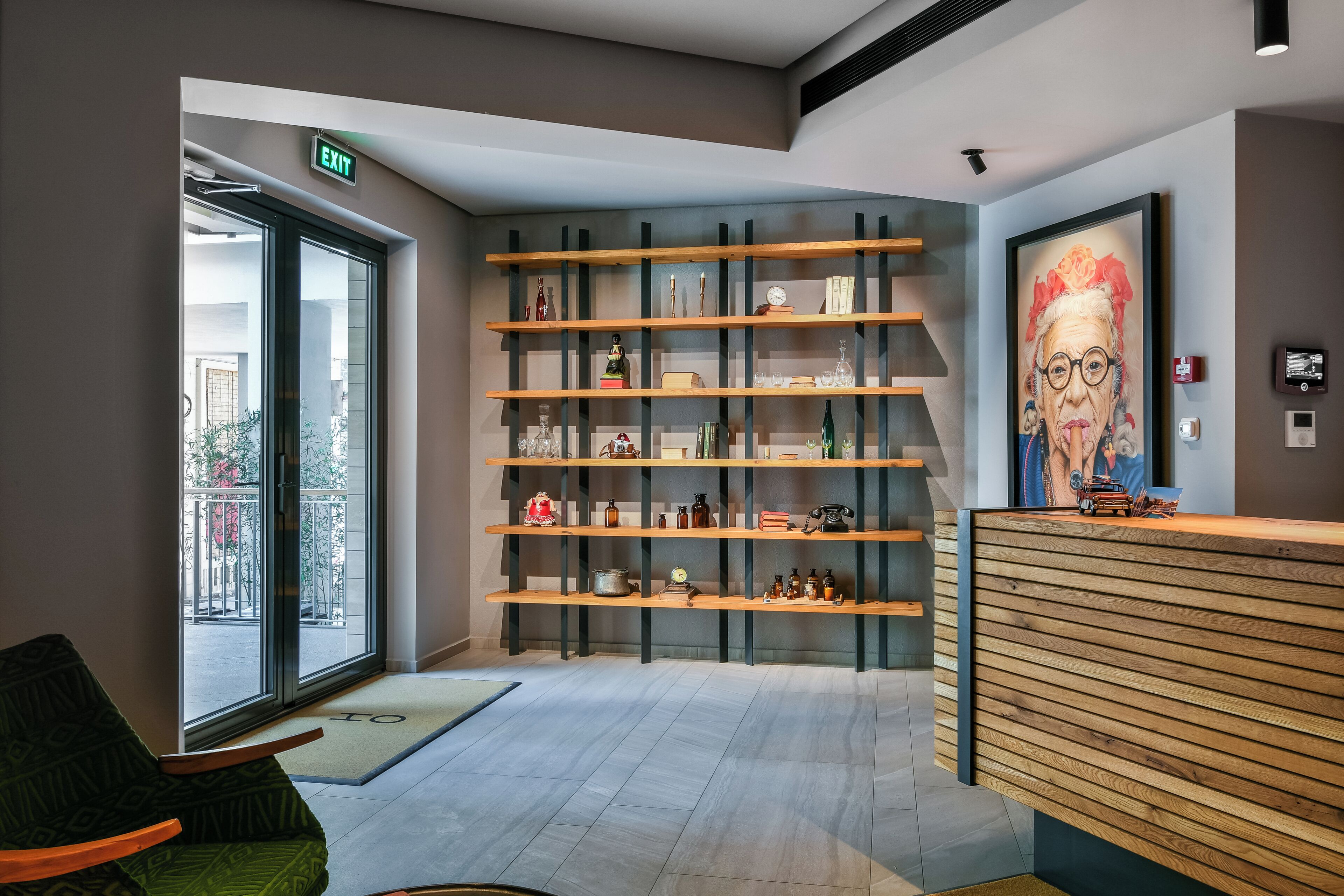 A reception area with a wooden reception desk, a glass door entrance, and a wall-mounted shelf with various items.