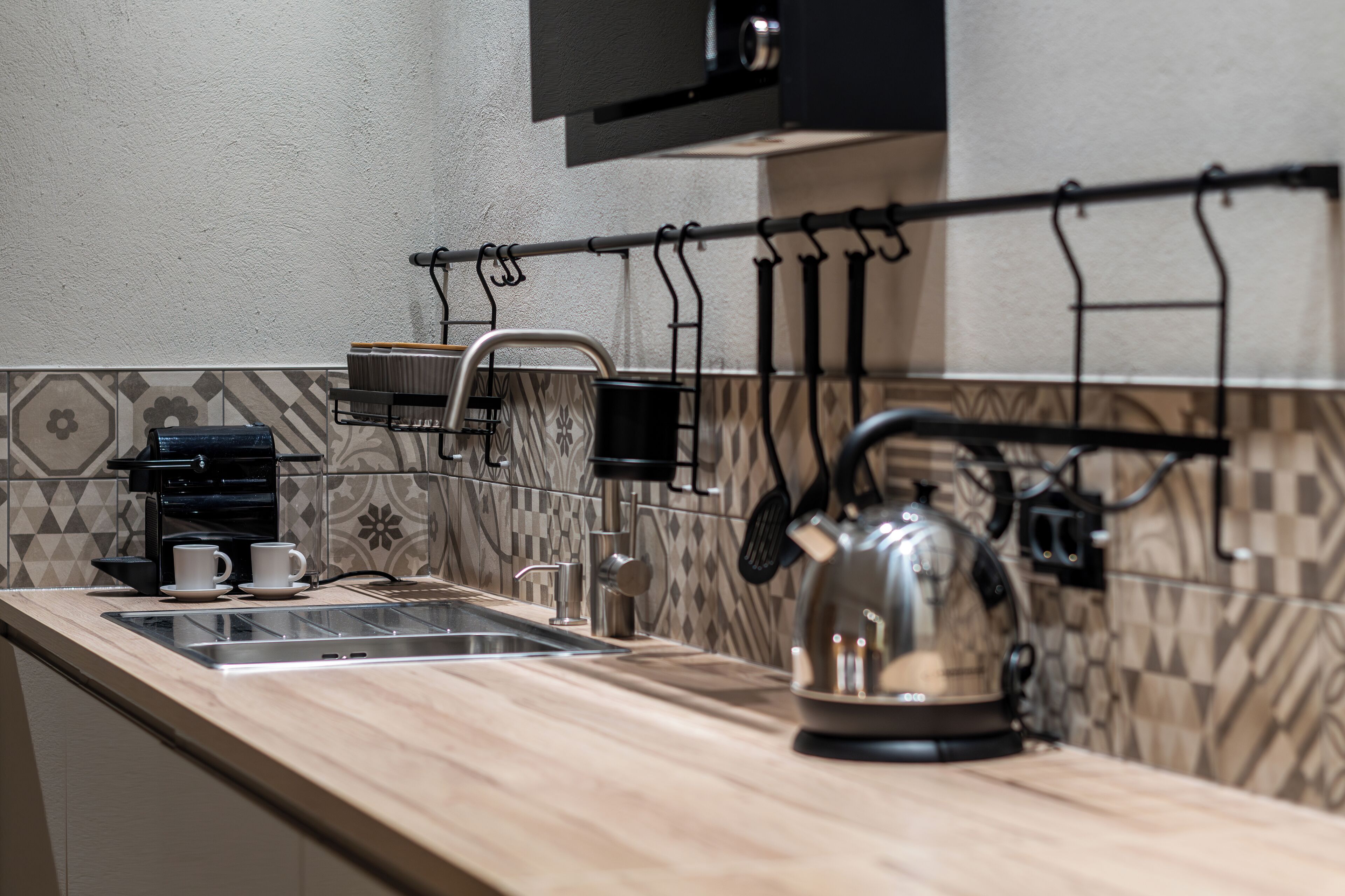 Una cocina con mostrador de madera, hervidor, cafetera y un tendedero.