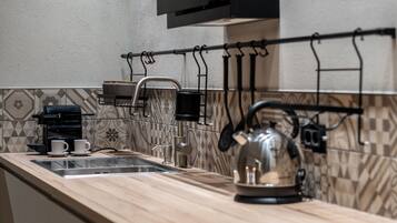 Una cocina con mostrador de madera, hervidor, cafetera y un tendedero.