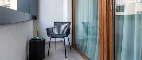 A balcony with a black chair, a small round table with a vase, and a sliding glass door with curtains.
