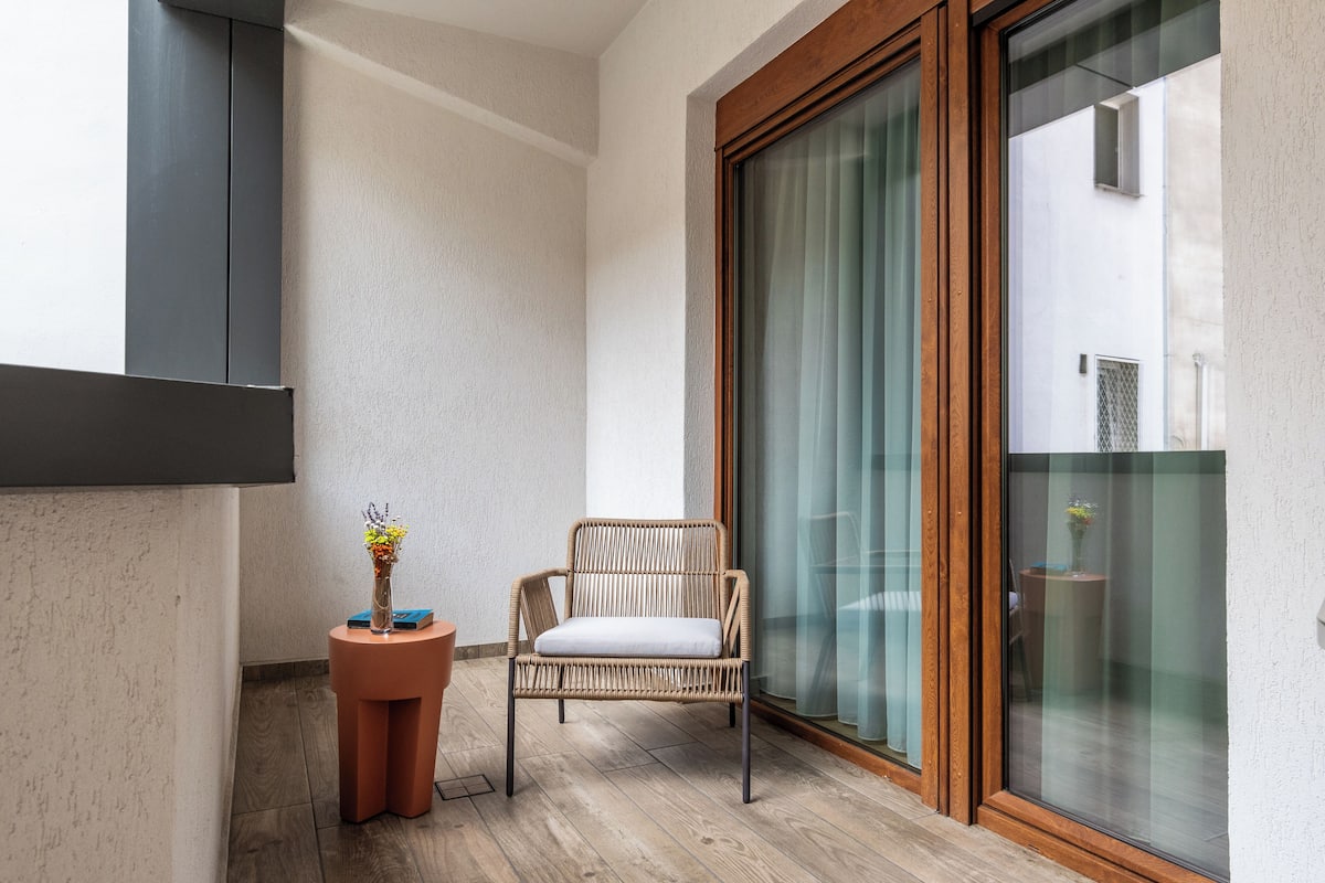 Un balcon avec un fauteuil en osier, une petite table ronde ornée d’un vase et une porte-fenêtre coulissante.
