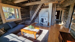 A log cabin interior with a sofa, coffee table, fireplace, and a staircase leading to an upper level. - Kaunisvirta villa for 10 with beautiful views. Pet-Friendly! (Pyhtään kirkonkylä)