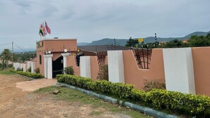 A building with a gated entrance, a flag on top, and a view of hills in the background. - JLK Guest House & Events Centre (Koforidua)