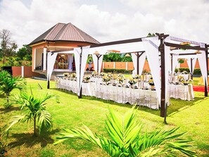 An outdoor wedding venue with a covered seating area, a stage, and a building in the background. - JLK Guest House & Events Centre (Koforidua)