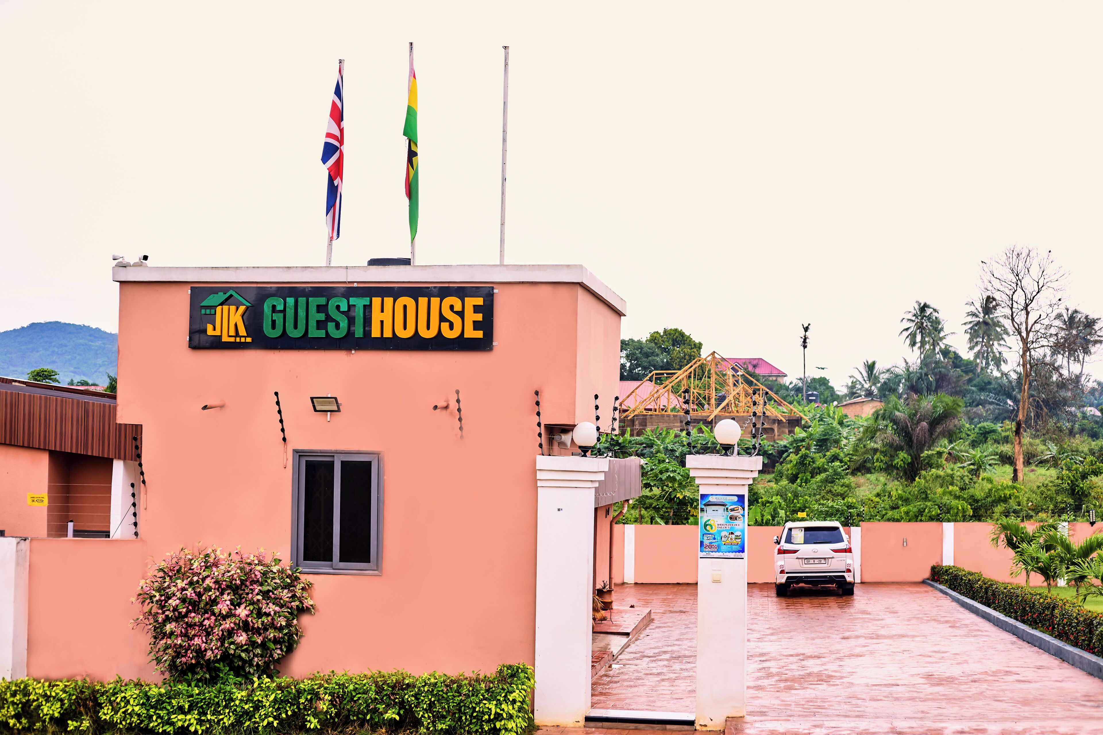 A building with a sign reading "JK GUESTHOUSE" and two flags on top.