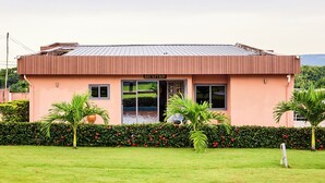 A building with a reception area, a metal roof, and a well-maintained garden with palm trees and hedges. - JLK Guest House & Events Centre (Koforidua)