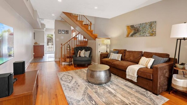 A modern living room with a brown sofa, a round coffee table, and a staircase leading to an upper level. - Fells Point Fenced in Yard Weber Gas Grill (Baltimore)