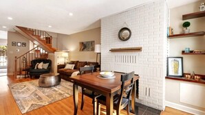 A dining area with a wooden table and chairs, a white brick wall, and a staircase leading to another room. - Fells Point Fenced in Yard Weber Gas Grill (Baltimore)
