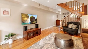 A living room with a wooden staircase, a television, a dark sofa, and a coffee table. - Fells Point Fenced in Yard Weber Gas Grill (Baltimore)
