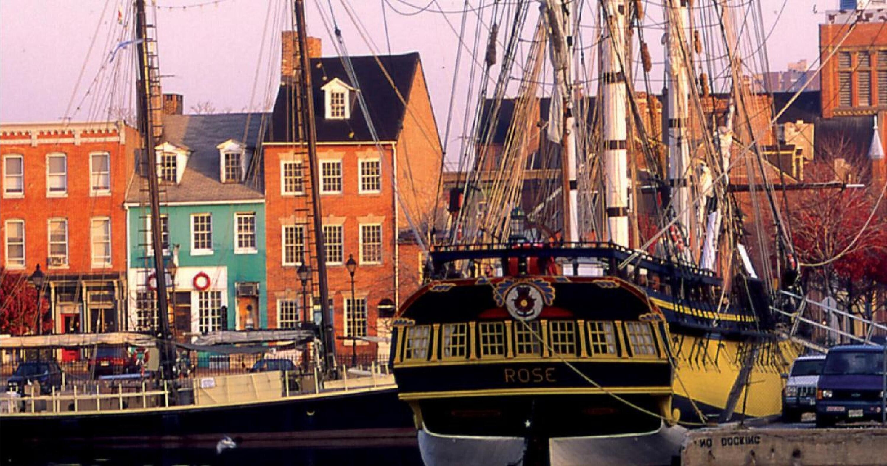A historic ship docked in a harbor with colorful buildings in the background.
