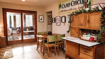 A cozy kitchen with wooden cabinets, a dining table with chairs, and a Christmas-themed sign.