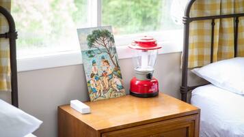 Une chambre à coucher avec une table de chevet, un tableau, une lampe rouge et blanche, et une fenêtre donnant sur des arbres.