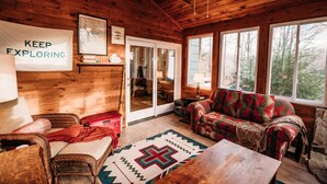 L’intérieur d’un chalet accueillant, avec un plafond en bois, une grande fenêtre, un canapé, une table et un tapis.