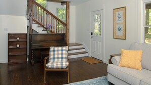 A living room with a wooden staircase, a white door, a gray sofa, and a blue rug.