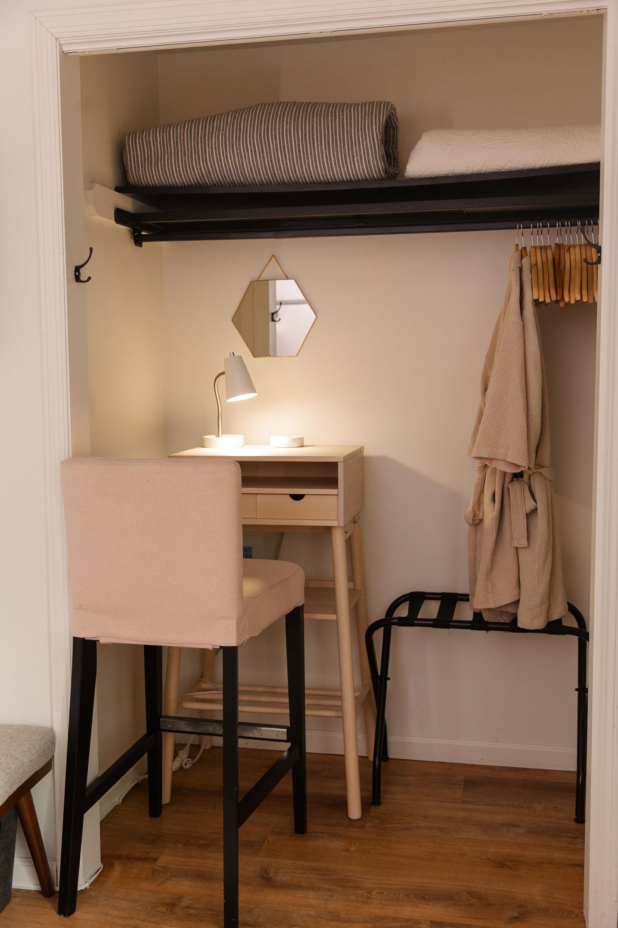 A compact bedroom with a bunk bed, a desk with a lamp, a chair, and a hanging robe.