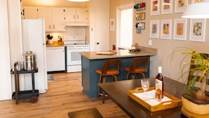 A kitchen with white cabinets, a central island with two chairs, a dining table with a tray, and a potted plant.