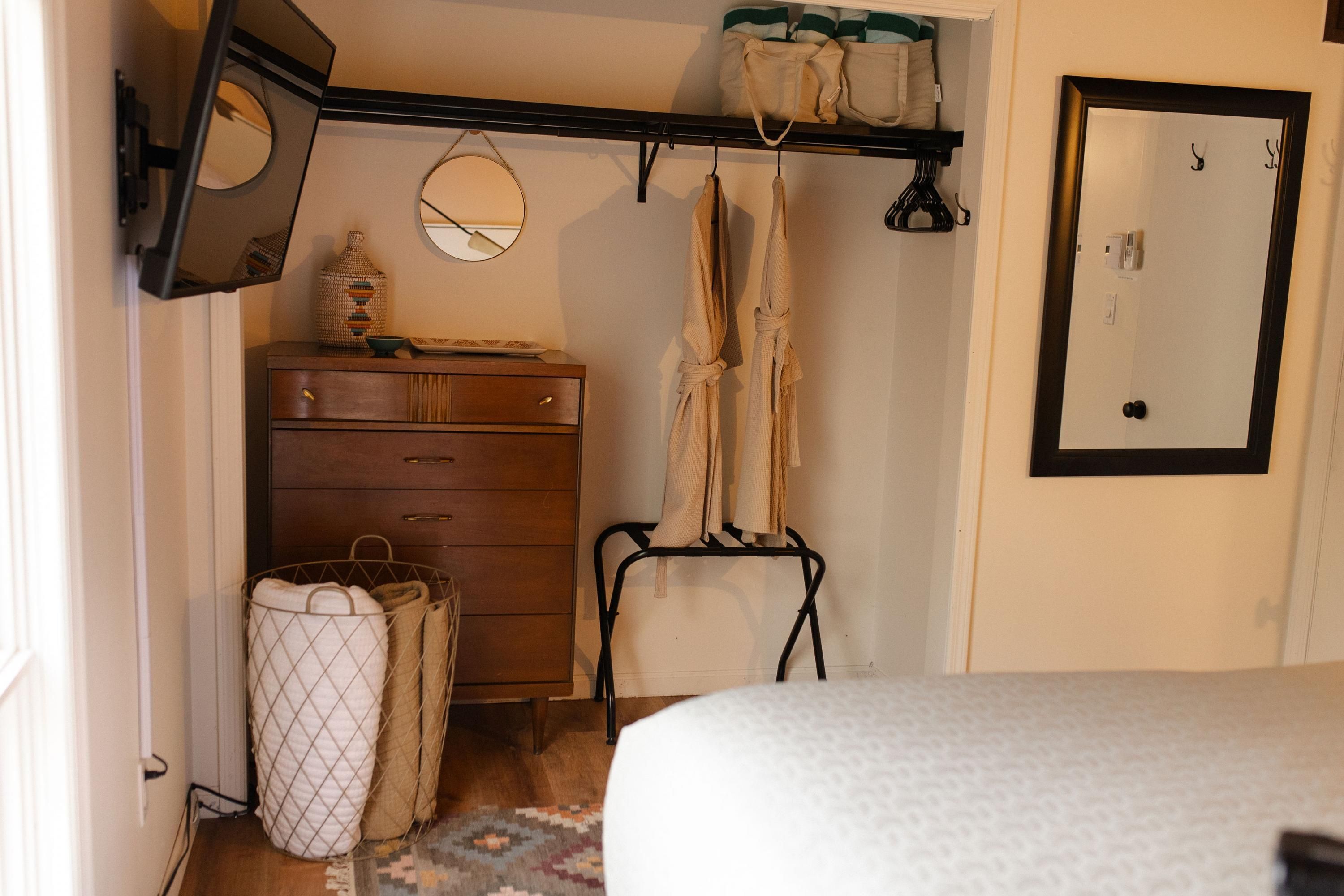 Un dormitorio con cama, cómoda, espejo y un perchero con toallas.