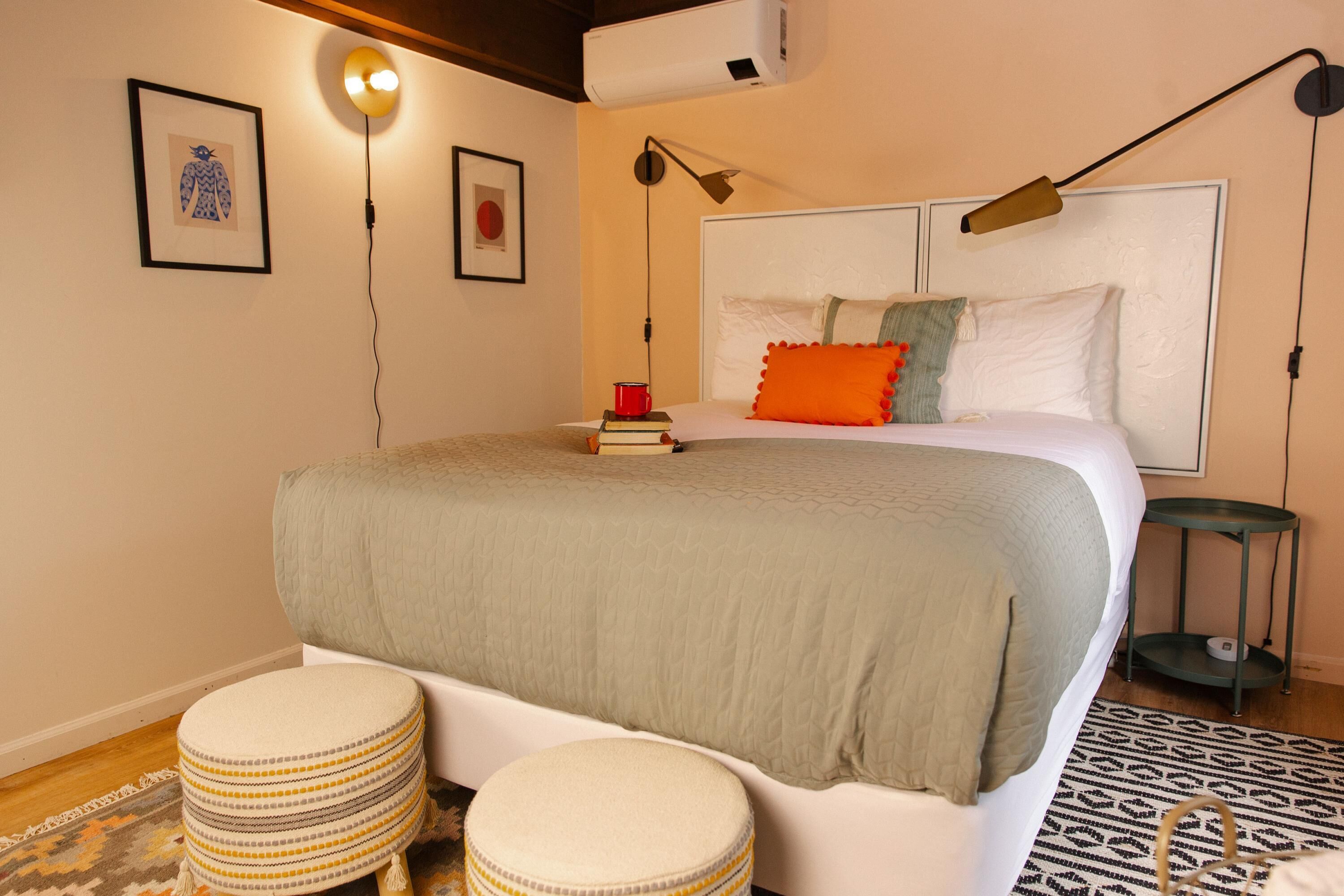 Une chambre à coucher bien aménagée, avec un grand lit, des lampes de chevet, une petite table et un climatiseur fixé au mur.