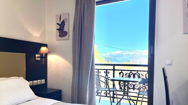 A hotel room with a bed, a nightstand, a lamp, a chair, a table, and a balcony with a view. - Vita Blu Studios (Zakynthos)