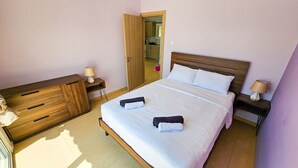 Un dormitorio ordenado con una cama, mesitas de noche, un aparador de madera y un baño visible a través de una puerta abierta.
