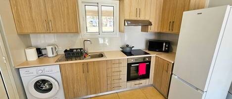 Een kleine keuken met houten kastjes, een magnetron, een spoelbak, een kookplaat en een wasmachine.