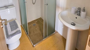 Un baño moderno con ducha de vidrio, lavamanos blanco y retrete.