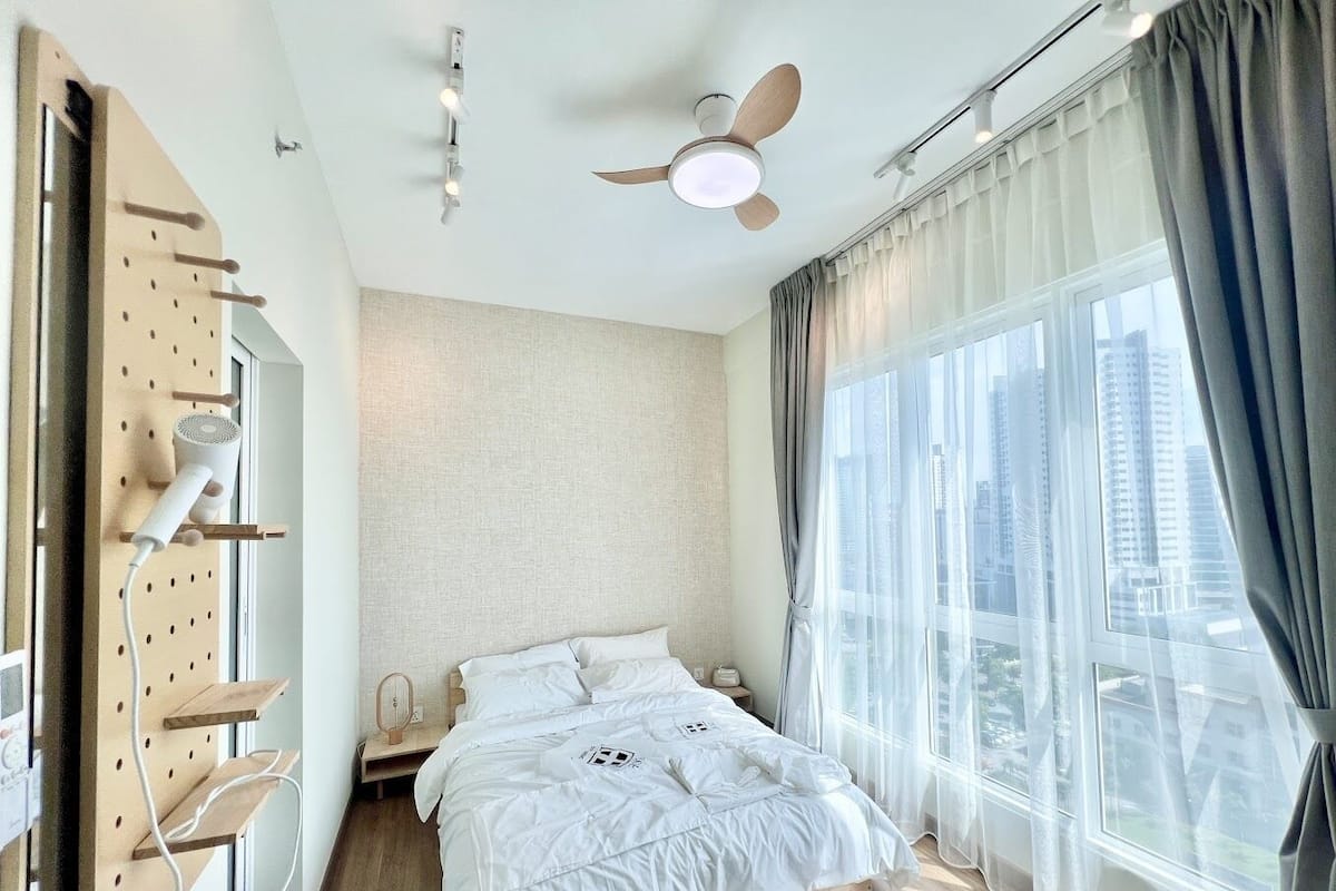 Ein modernes Schlafzimmer mit einem Bett, einem Deckenventilator, einem Fenster mit Vorhängen und einem an der Wand befestigten Wäscheständer.
