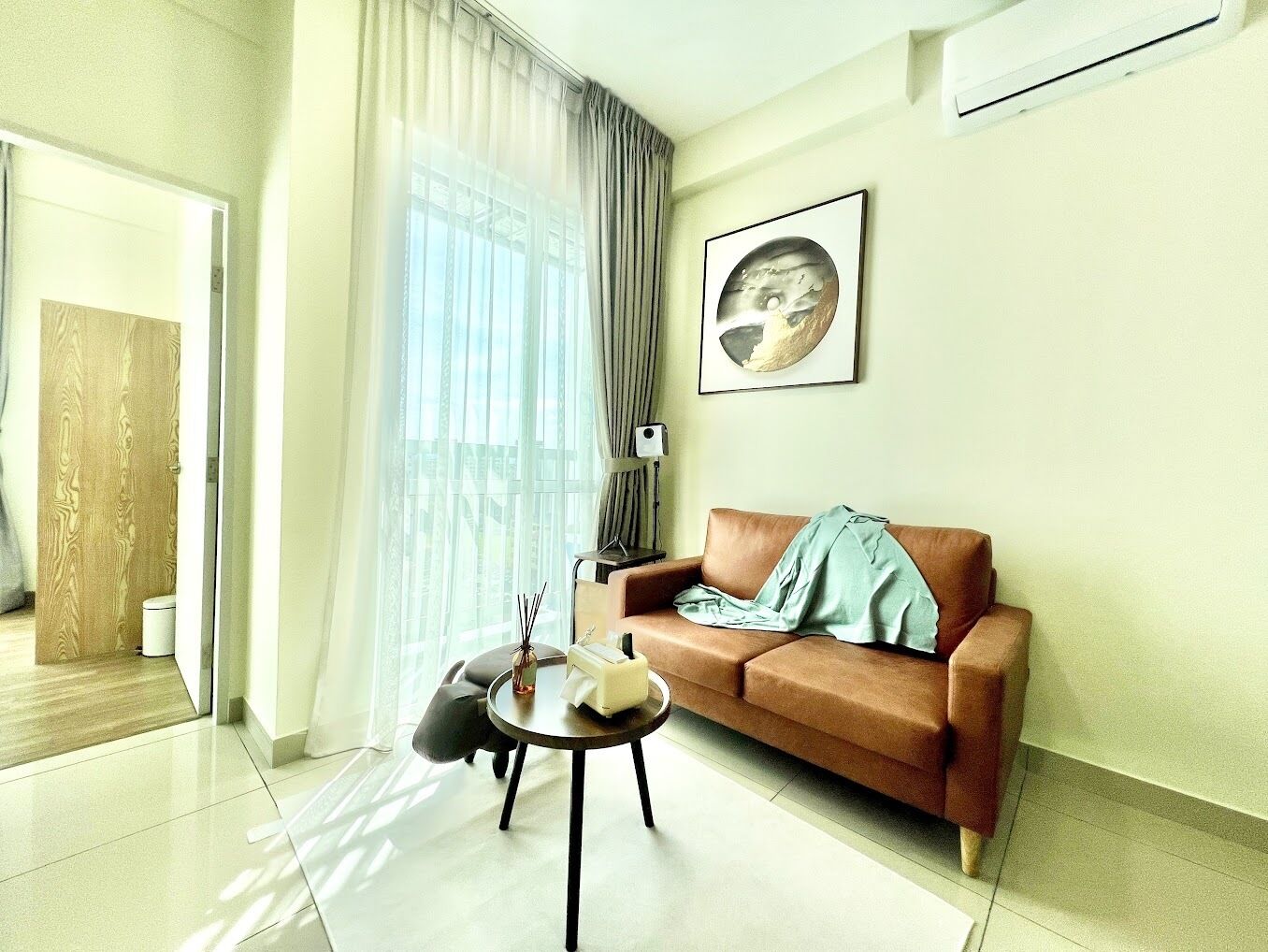 A modern living room with a brown sofa, a round coffee table, and a large window with sheer curtains.