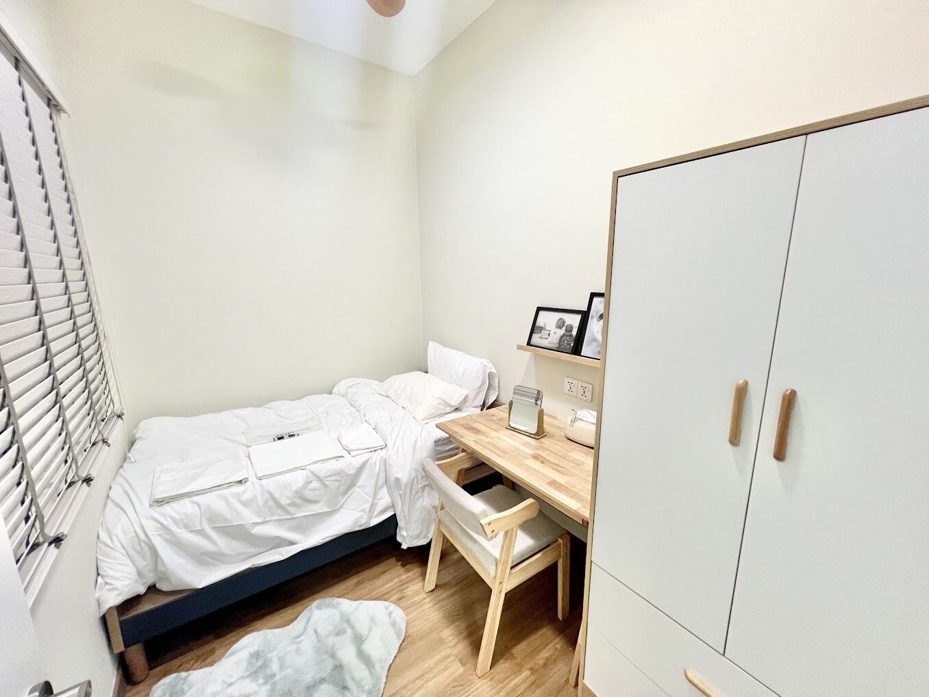 A small, neatly arranged bedroom with a bed, a wooden desk, a chair, and a wardrobe.
