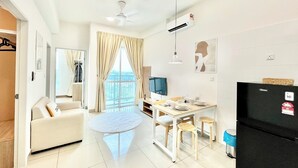 A modern living room with a sofa, a dining table with chairs, a ceiling fan, and a large window with curtains. - Plaza Kelana Jaya by Sleepy Bear (Petaling Jaya)