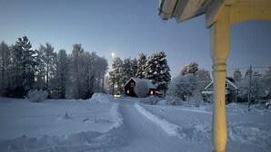 A snow-covered landscape with a wooden house and a snow-covered path leading to it.