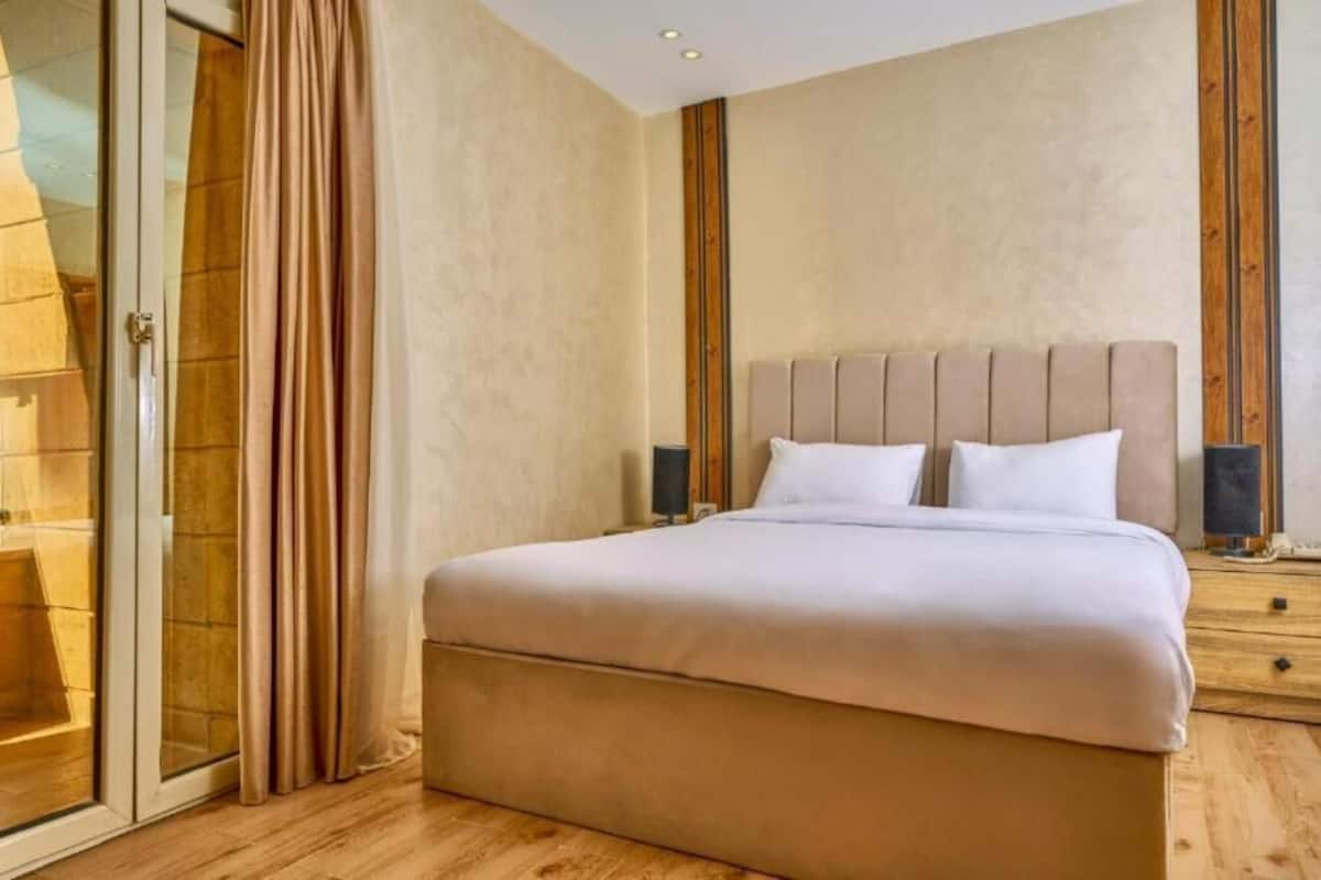 Quarto com cama grande, mesa de cabeceira de madeira e porta de vidro deslizante.