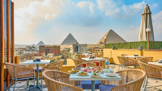 A rooftop dining area with tables and chairs, a view of the pyramids, and a cityscape in the background. - Cleopatra Tower Pyramids Hotel (Giza)