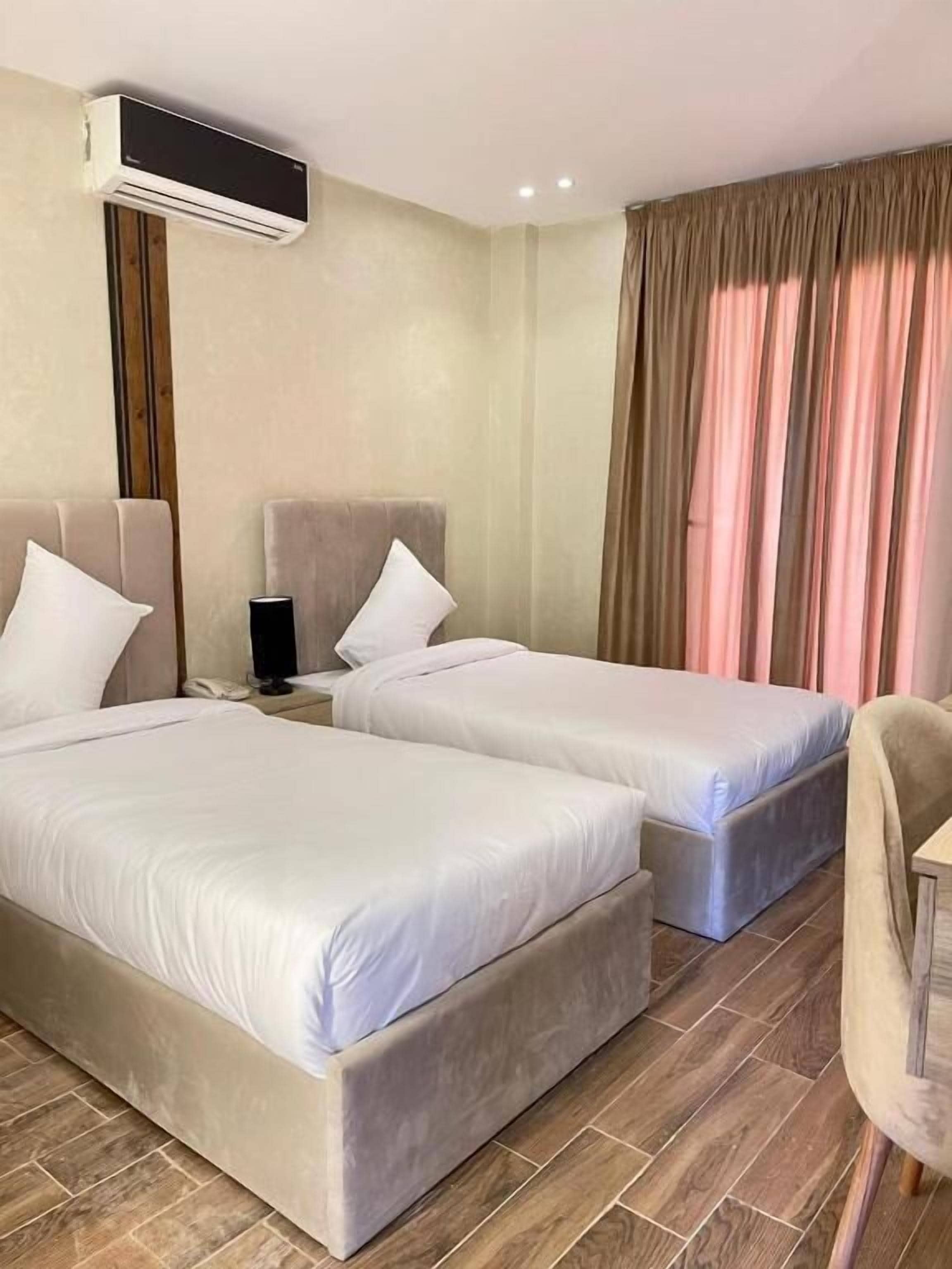 Habitació d'hotel amb dos llits, una taula de nit amb una làmpada, un telèfon i un aparell d'aire condicionat a la paret.