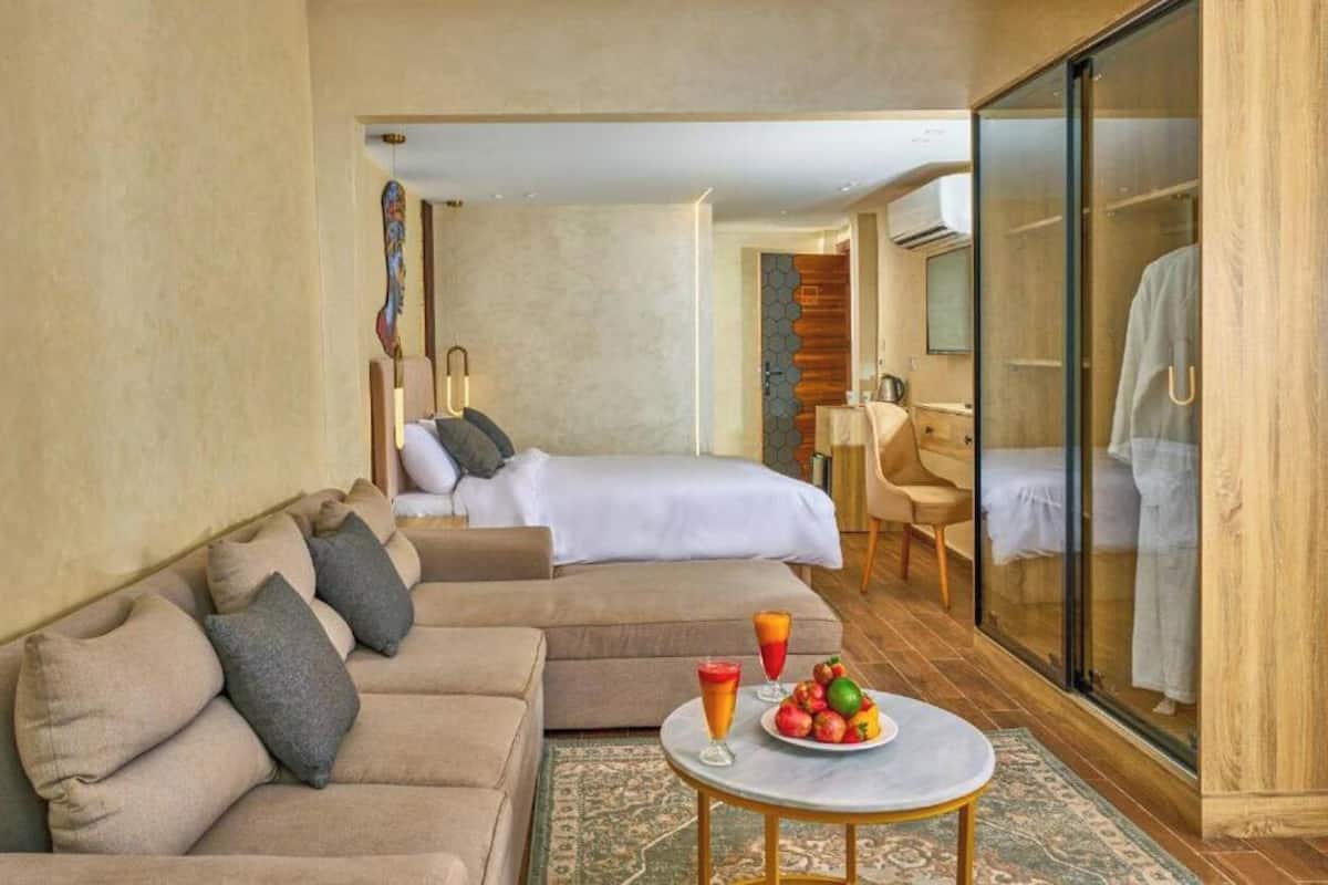 Quarto de hotel com sofá, cama, box de vidro e uma mesinha com frutas.
