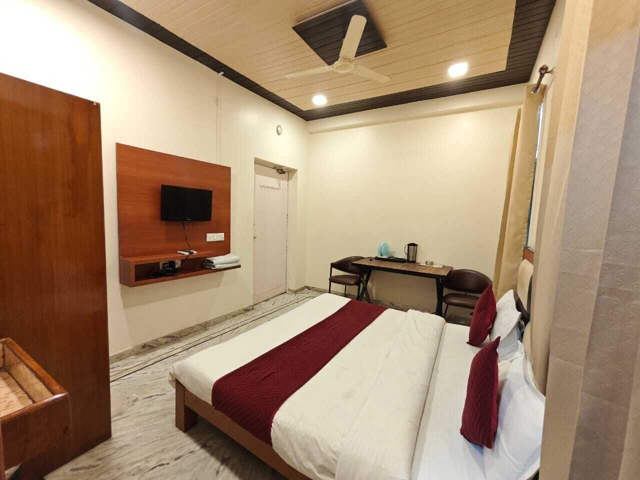 A hotel room with a bed, a desk, a chair, a television mounted on the wall, and a ceiling fan.