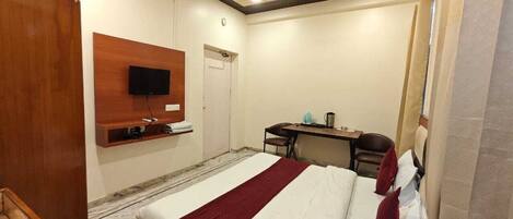 Habitación de hotel con cama, escritorio, silla, televisión montada en la pared y ventilador de techo.