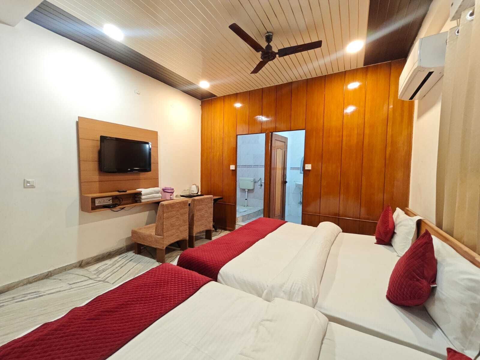A hotel room with two beds, a TV mounted on the wall, a ceiling fan, and an air conditioning unit.