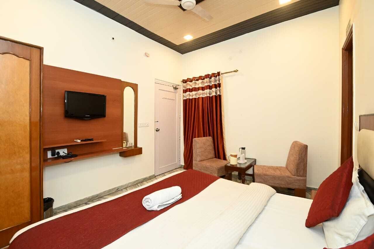 Hotelkamer met een bed, een aan de muur bevestigde televisie, een stoel en een tafeltje met een lamp.