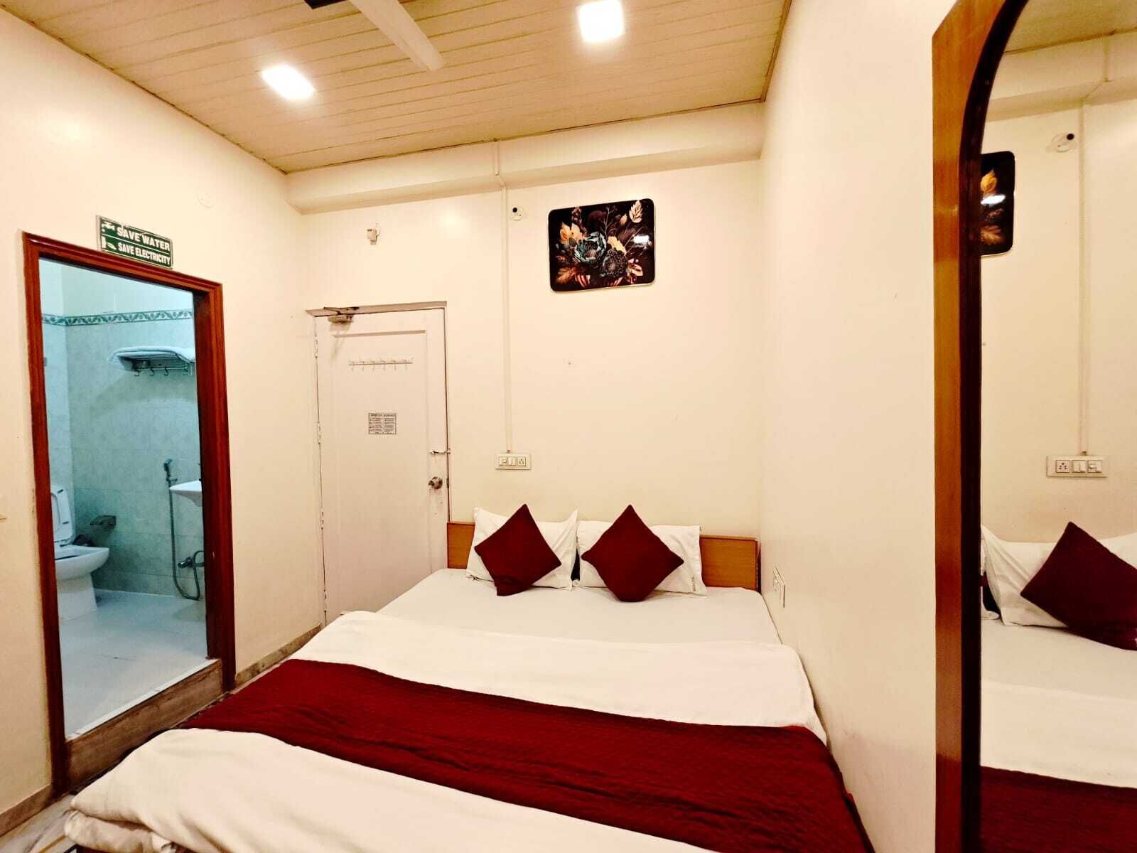 Una habitación de hotel con cama, espejo, puerta y un pequeño cuadro en la pared.