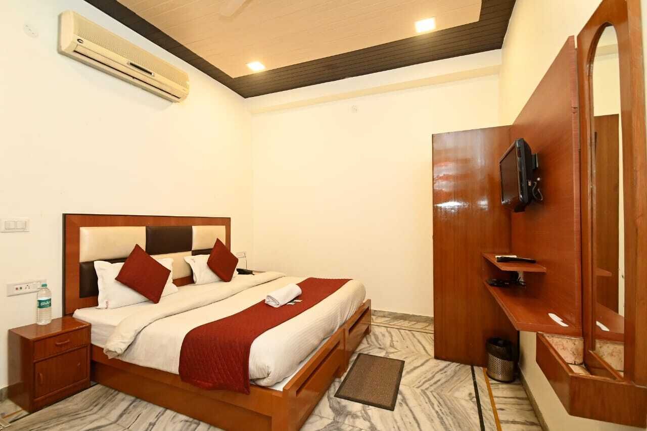 A hotel room with a wooden bed, a TV mounted on the wall, a small bedside table, and a marble floor.