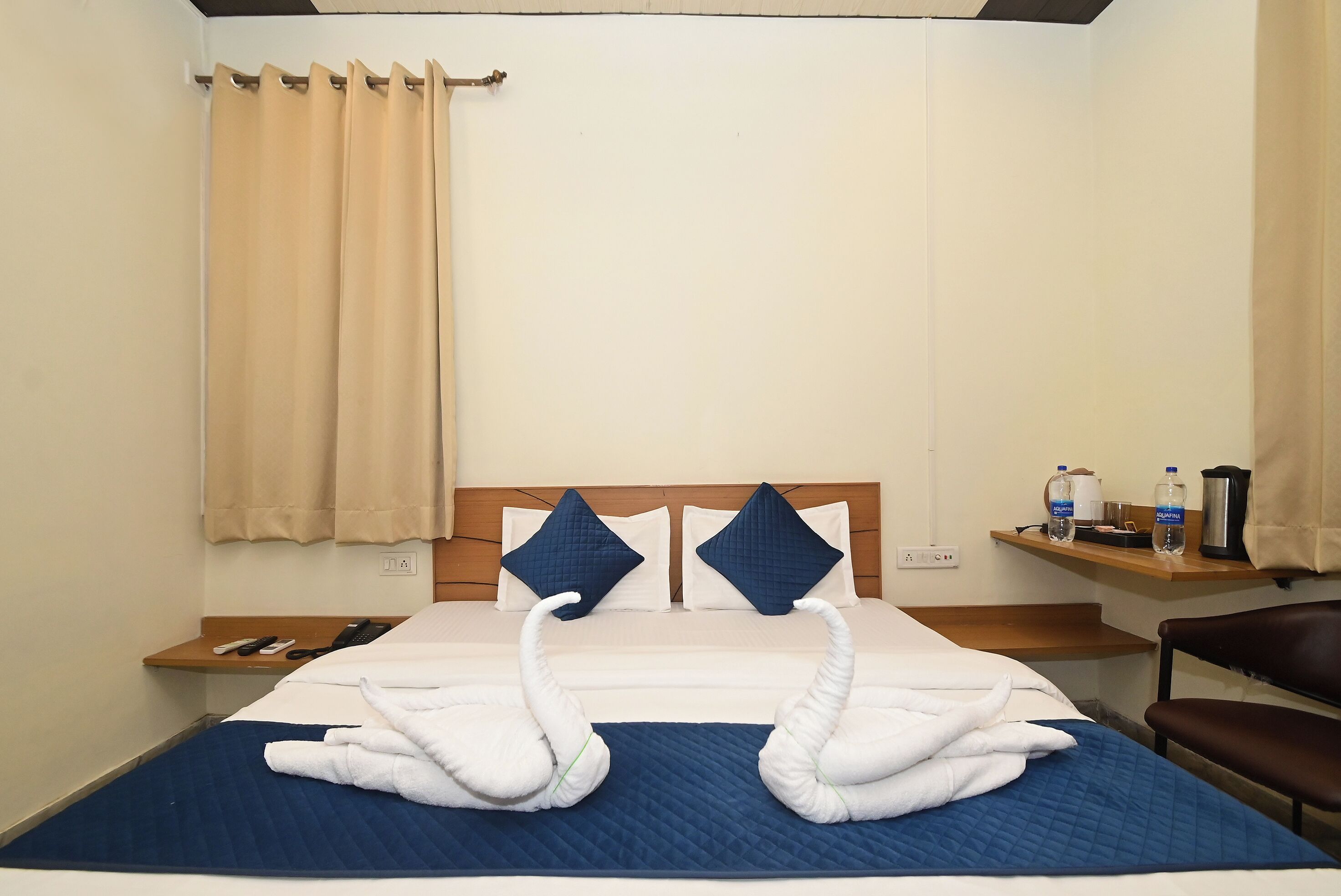 Ein Hotelzimmer mit einem Bett, zwei Kissen, einem Nachttisch, einem Stuhl und einem Regal mit Gegenständen.