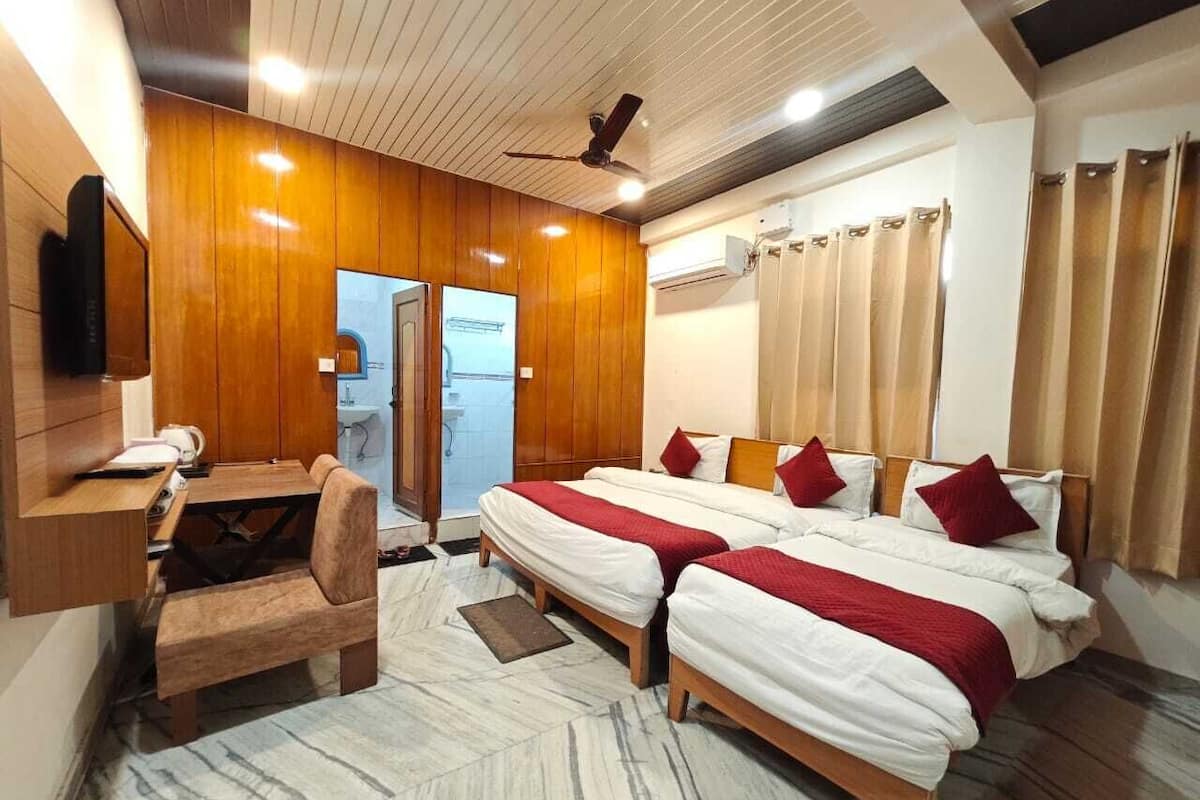Habitación de hotel con dos camas, un escritorio, una silla, un televisor y zona de ducha.