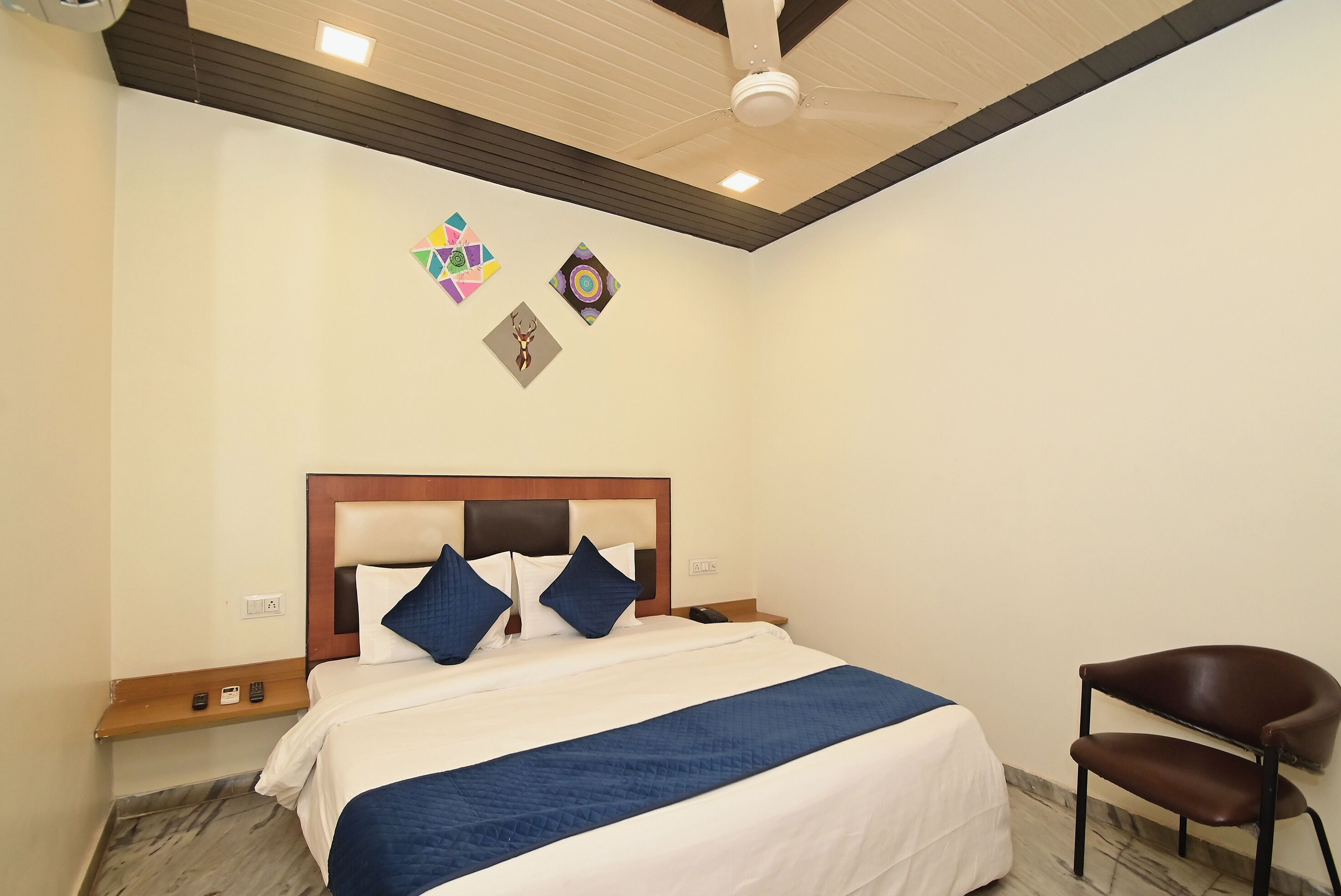 A hotel room with a bed, a chair, a ceiling fan, and wall decorations.