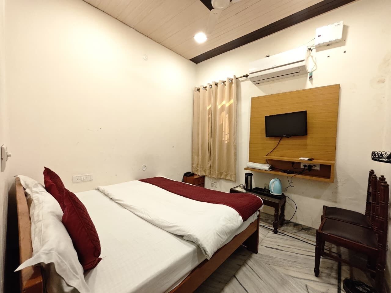 Habitación de hotel con una cama, televisión montada en la pared, escritorio con silla y aire acondicionado.