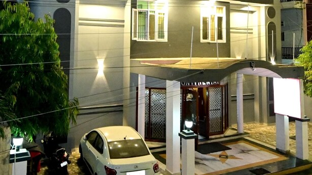 Un hotel de varios pisos con fachada moderna, un acceso cubierto y un coche estacionado frente al edificio.