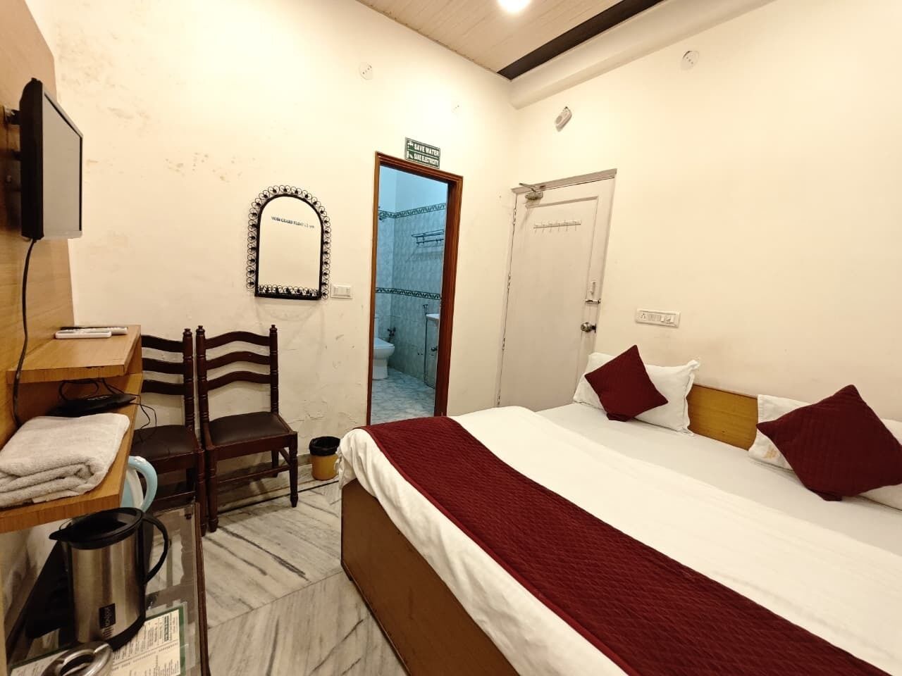 Habitación de hotel con una cama, una silla, un escritorio con computadora, un espejo y una puerta que da a un baño.